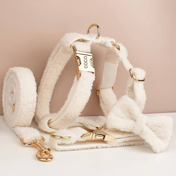 Product shot of the full set of white furry white dog's harness, collar, leash and bow-tie against apricot background